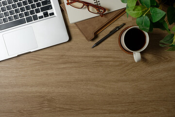 Wall Mural - Top view of modern wooden desk with laptop, notebook, coffee cup, and eyeglasses in natural lighting.