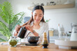 © wattana - Young woman preparing matcha tea in a bright modern kitchen, pouring hot water into a traditional bowl.