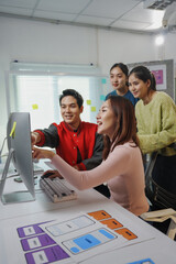 Team of asian software developers working together analyzing user interface design of mobile application on desktop computer