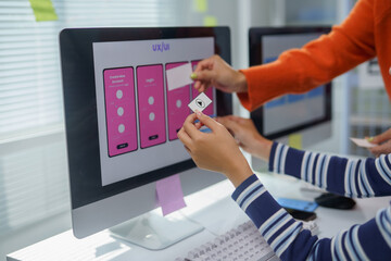 web designers working together positioning icons on a mobile app interface displayed on a desktop co
