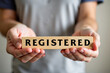 © Creuxnoir - Person holding a wooden block with word 'registered' written on it, against a blurred background.