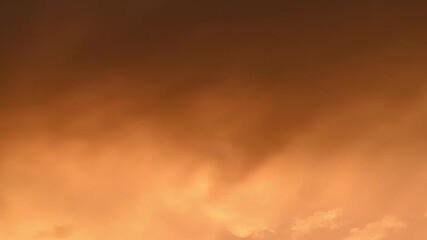 Wall Mural - Timelapse of late day orange smoke-like clouds drifting across the sky and slowly changing to shades of pink
