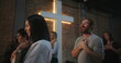 © Marco - Diverse group of people participating in a Christian worship ceremony, some standing with hands clasped in prayer, glowing cross in the background