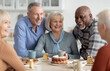 © Prostock-studio - Cheerful senior people of different nationalities sitting at kitchen, drinking tea and eating cake together, having conversation and laughing, chilling together at nursing home