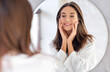 © Prostock-studio - Skincare Concept. Pretty Young Woman Touching Her Face While Looking At Mirror In Bathroom, Attractive Female Smiling To Reflection, Enjoying Skin Condition After Beauty Treatments, Selective Focus