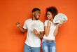 © Prostock-studio - Big luck. Cheerful african-american young man and woman enjoying lots of money, orange background