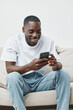© SHOTPRIME STUDIO - Smiling young man using smartphone at home, wearing casual white t shirt and jeans, creating a relaxed atmosphere, perfect for social media engagement