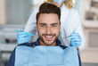 © Prostock-studio - Smiling young bearded man sitting in dental chair, visiting modern dental clinic, having regular checkup, unrecognizable woman dentist holding dental tools next to male patient mouth