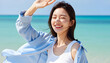 © minwoo Jung - 밝은 여름 햇살 아래 해변에서 미소 짓고 있는 젊은 여성 모델, 흰색 민소매와 파란 셔츠를 입고 자연스럽고 상쾌한 분위기