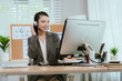 © Witoon - Smiling Asian female call center agent wearing a headset, speaking with a client at her office desk, providing professional customer support.