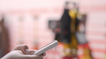 Person is holding a cell phone and looking at it. The phone is white and the person is wearing gloves