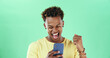 © peopleimages.com - Black man, phone and celebration in studio with fist pump, success and win online prize by green background. African person, smartphone and mobile app with goals, profit and mockup space with trading