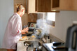 © shintartanya - Young woman working remotely from the kitchen, balancing cooking and video call, enjoying mindful morning routine and modern lifestyle. Home office, wellness, healthy habits.