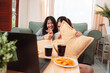 © Kiattisak - Asian Women Snack Food Eating Lifestyle Indoor Living Room Enjoyment Movie, Two Young Adults Sharing Laughter and Snacks While Watching TV, Embracing Friendship and Relaxation at Home Together