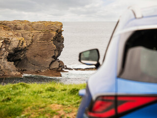Wall Mural - A blue car is parked on the side of a road next to a cliff overlooking the ocean. Travel and tourism. Trip to nature, cloudy day, rough stone coast. Sightseeing landmarks. West of Ireland.