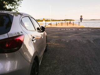 Wall Mural - Small car parked by a pier on a lake in a shadow. Nobody. Travel and tourism. Copy space. Warm sunny background. Hot holiday season concept.