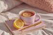© whitestorm - A cozy and calming image of a pink mug of tea with lemon, placed on a pink notebook next to a golden pen, on a soft white bed with a pink pillow.