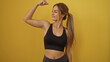 © Krakenimages.com - Woman flexing arm against vibrant yellow background showing strength and confidence in athletic attire with a proud expression highlighting empowerment and fitness.