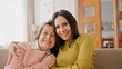 © VAKSMANV - Warm moment of happy Caucasian family hugging each other. Beautiful girl embracing her mature mother while sitting together on sofa. Loving relatives happy about pleasant meeting at home. Relatives.