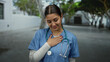© Krakenimages.com - Young woman in scrubs with stethoscope outdoors shows gratitude, blending medical professionalism in an urban setting.