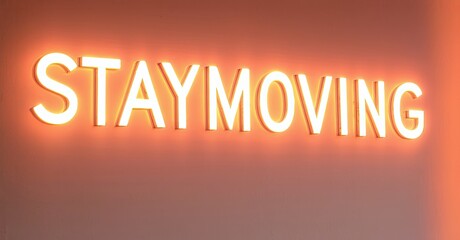 Poster - Bright neon sign displays STAYMOVING. Warm orange glow illuminates surrounding surface. Minimalist design, motivational message.