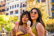 © unai - Two happy women eating ice cream in a city center during summer