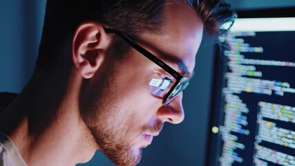Poster - Young man with glasses coding at computer in modern workspace, technology at night, intense concentration, blue light reflecting