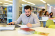 © JackF - Focused guy student studying at the university studies in the library on a laptop while preparing for the exam, making ..important notes in a copybook
