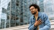 © Marius - Man Clutches His Chest in Pain While Seated Outside a Modern Building with Glass Facade