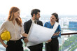© Jack Tamrong - Architect man holding project blueprint two female colleagues working together at high rise office balcony