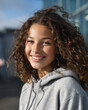 © mittpro - Beautiful smiling teenage girl with curly brown hair wearing a grey hooded sweatshirt outdoors