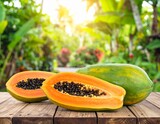 Ripe cut papaya fruit on the wooden table on green jungle background. 
