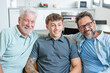 © luciano - Happy multigenerational family of males stay together sitting on sofa smiling. Grandfather, mature son and young grandson share positive moments in total relax