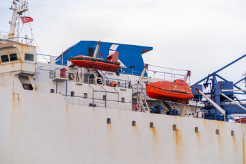 Poster - View of a cargo ship at Bosphorus with lifeboats prepared for emergency situations and colorful structures against a cloudy sky