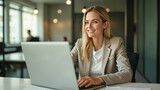 Blond kobieta pracująca przy laptopie w jasnym biurze. Styl casual business, lekki uśmiech, realistyczne zdjęcie z miękkim światłem i profesjonalnym wnętrzem korporacyjnym.