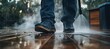© Naim - Person Using High-Pressure Power Washer to Clean Wooden Backyard Floor