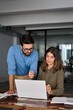 © insta_photos - Young male manager helping mature female employee explaining software using laptop working together in office. Happy busy professional business people discussing computer work in office. Vertical