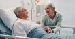 © peopleimages.com - Senior woman, man and holding hands in hospital bed for care, love or support for healing process. Elderly people, couple and kindness for trust, smile or visit patient for rehabilitation at clinic