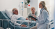 © Wesley25/peopleimages.com - Hospital bed, doctor and senior man with wife for support, comfort or empathy with medical diagnosis. Conversation, healthcare and elderly male patient with woman and surgeon for feedback on surgery.