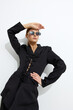 © SHOTPRIME STUDIO - Stylish woman in black lace-up blazer and sunglasses poses confidently against white background, showcasing modern fashion and minimalistic elegance.