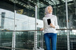 © Chanakon - Muslim asian businesswoman traveler holding boarding pass ticket, passport and smartphone at the airport terminal with her luggage. Islamic cheerful tourist female having holiday trip weekend.