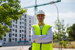 © pedro - Professional young male construction worker with safety helmet and reflective vest at a construction site with building progress in the background