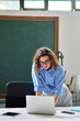 © insta_photos - Young happy woman school professional online teacher standing at desk in classroom working on computer teaching remote education. Female employee or coach using laptop in corporate office. Vertical
