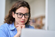 © insta_photos - Busy young serious professional business woman employee or student wearing glasses using laptop watching online webinar or training web course, looking at computer, thinking, elearning. Close up
