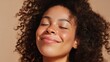 © tao - Black woman with curly afro hair, eyes closed, smiling gently against beige background, showing loose flowing hair around face, natural makeup, radiant skin glow, photo taken from above angle.