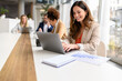 © Moon Safari - Smiling businesswoman working on project over laptop with colleagues during collaborative meeting in office