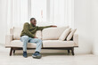 © SHOTPRIME STUDIO - Comfortable young Black man relaxing on a beige sofa in a bright and modern living room, wearing casual clothing, with a calm and satisfied expression