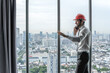 © Jack Tamrong - Handsome Caucasian male architect with safety helmet standing in high rise office talking on phone with skyscraper downtown view background