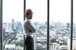 © Jack Tamrong - Handsome Caucasian male architect with safety helmet standing in high rise office with skyscraper downtown view background