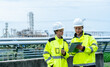 © narong - Man and woman of petrochemical or gas factory workers discuss about work with document pad and stand in front of pipeline of factory.